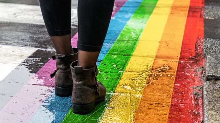 A person's feet walking on a crosswalk painted like a rainbow, in the rain