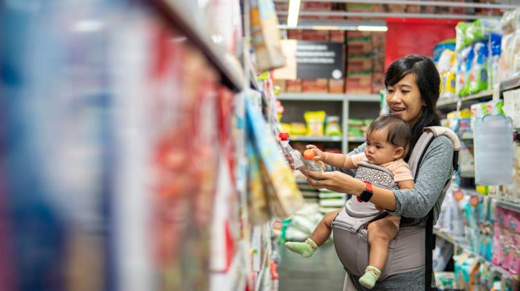 A mom shopping with her baby in a drugstore aisle, as the baby grabs at a product container.
